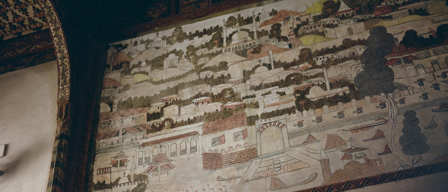 Historical wall mural of a city landscape with white houses, domes, and trees