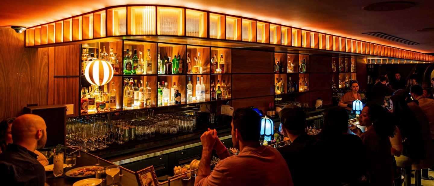 Busy bar with warm lighting and wooden shelves filled with bottles