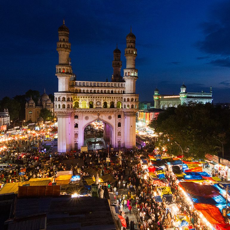 Aerial view of the bustling night market at the historic Charminar in Hyderabad, India, illuminated under the evening sky.