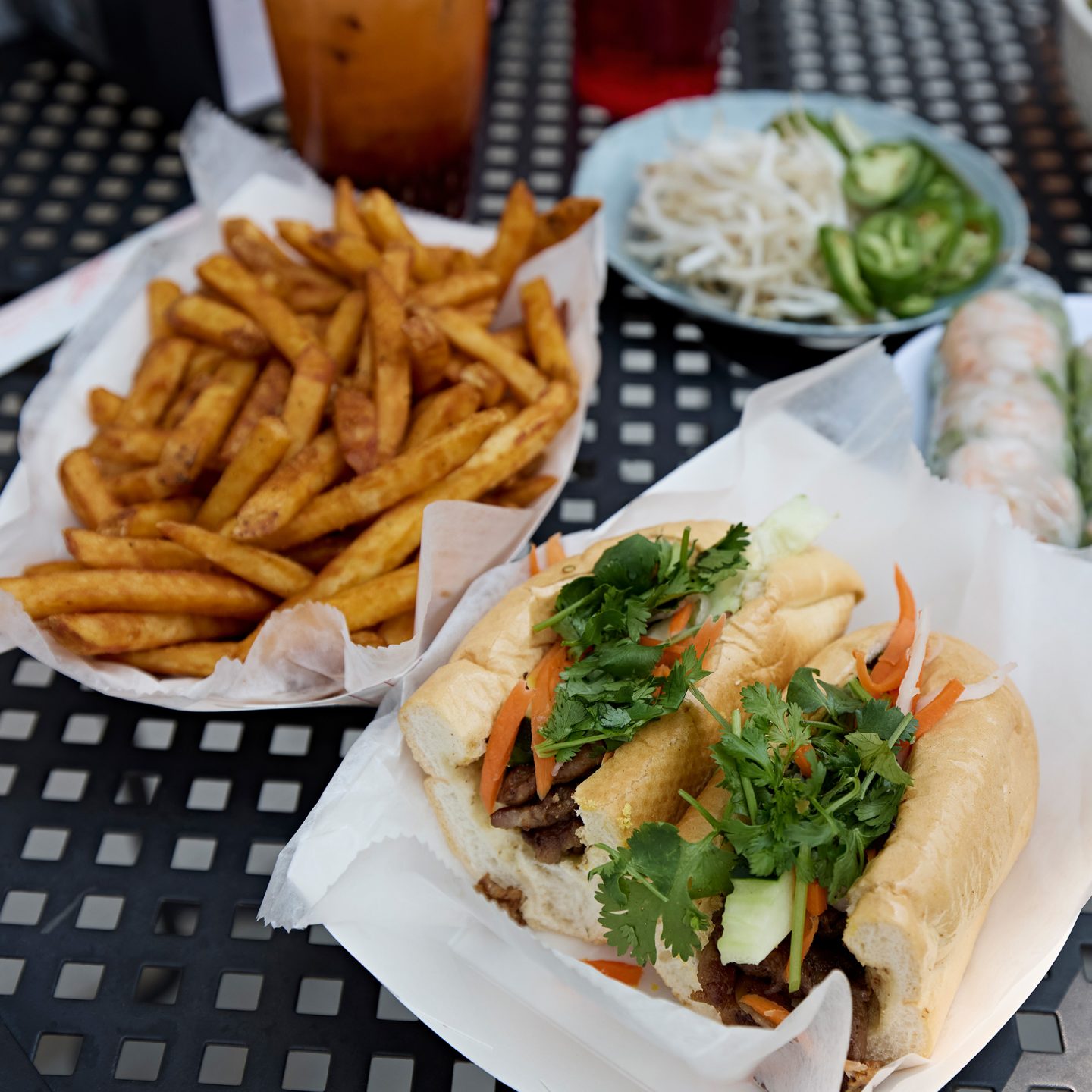Bánh mì, fries, and spring rolls on black table with dipping sauce and jalapeños