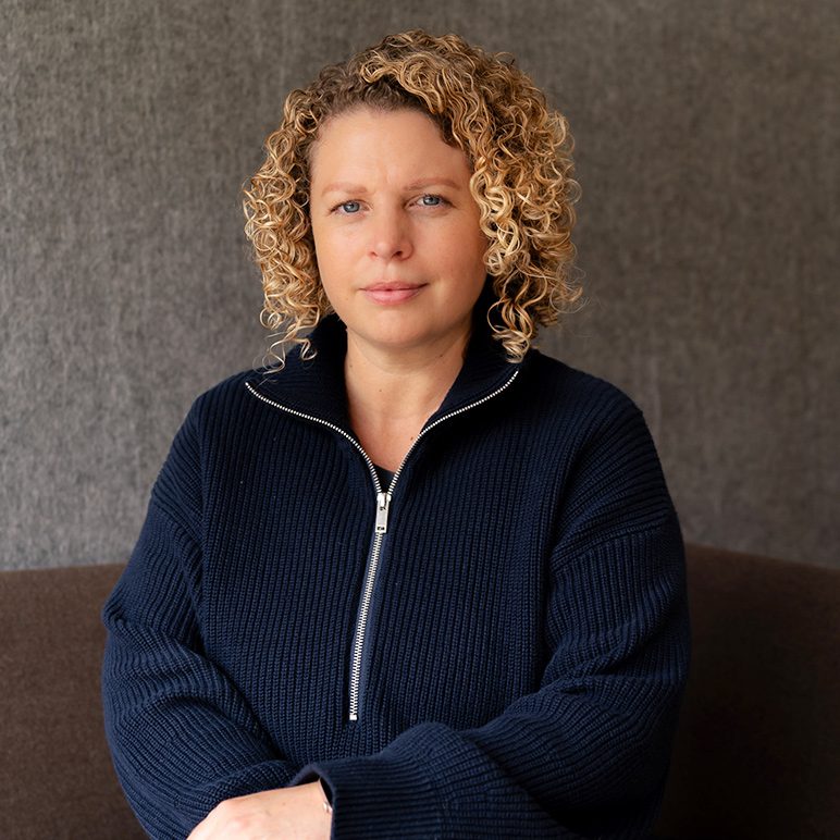 Portrait of Jenny Southan with blonde curly hair wearing a dark blue ribbed sweater