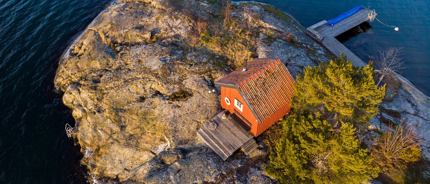 Aerial view of a small red wooden cabin on a rocky island with a private jetty