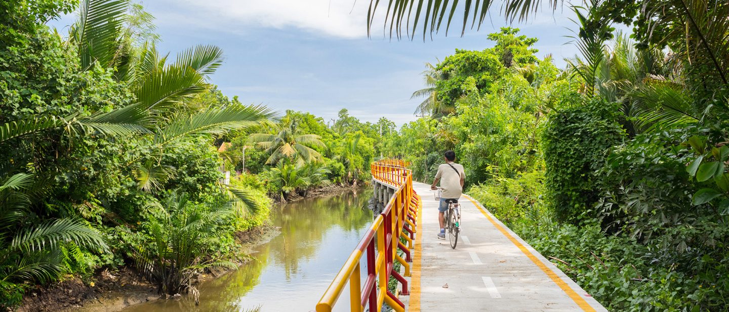 Man biking on a colorful bridge surrounded by lush greenery and a calm river.
