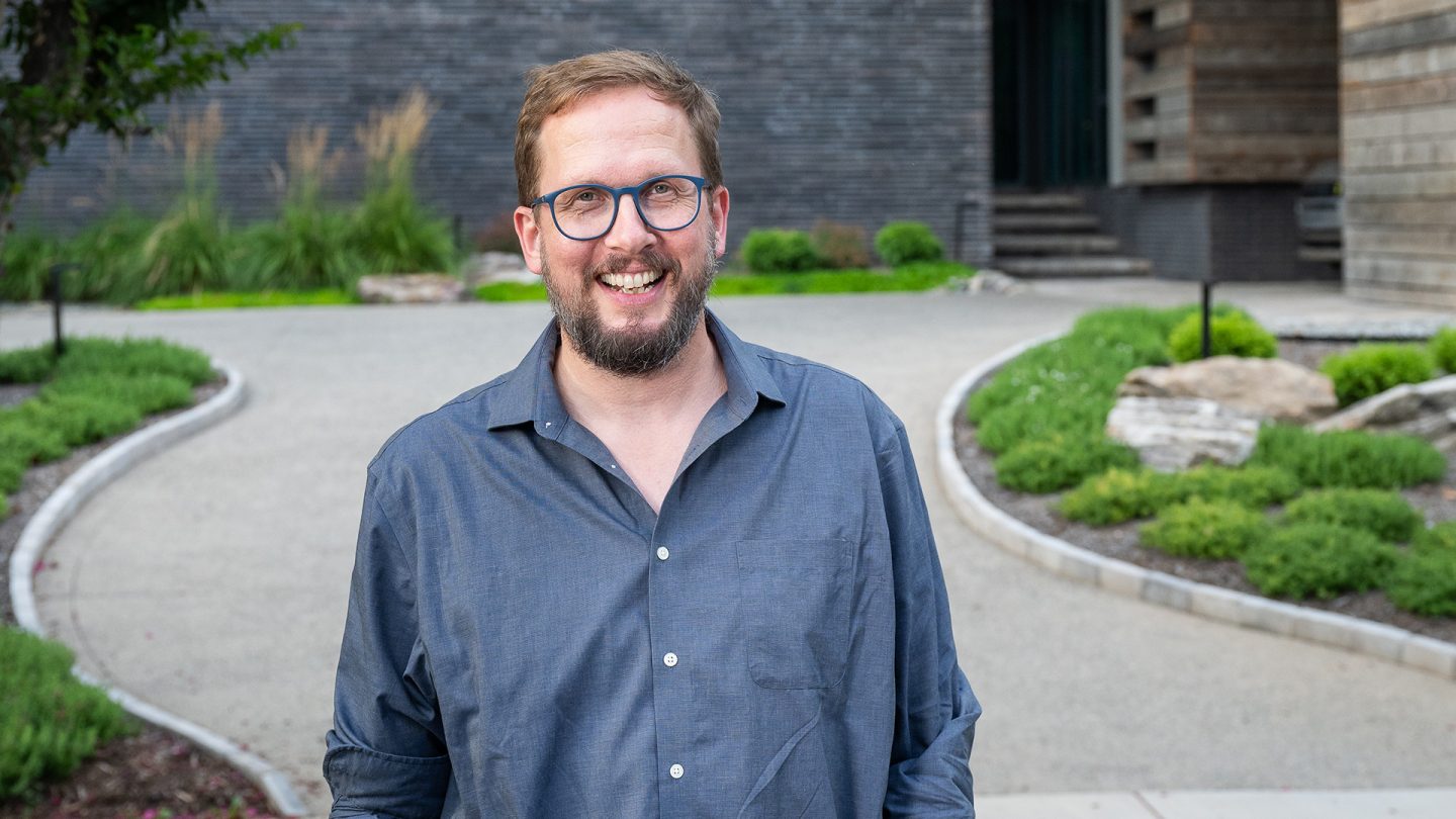 Architect Toby Witte smiling outdoors with a curved walkway and lush greenery in the background