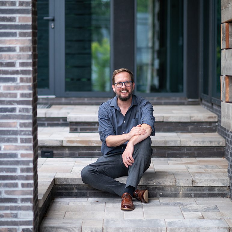 Toby Witte sits relaxed on stone steps in front of a modern building with dark facade