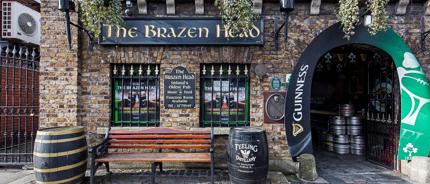 Exterior view of The Brazen Head, Ireland's oldest pub, with signage, benches, and barrels