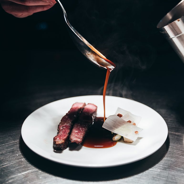 Dark sauce being poured over roasted meat on a plate at the Betong restaurant in Bjørvika