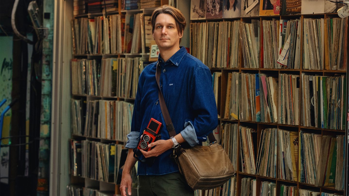 Tim Franco with a camera in his hand in front of a shelf with records