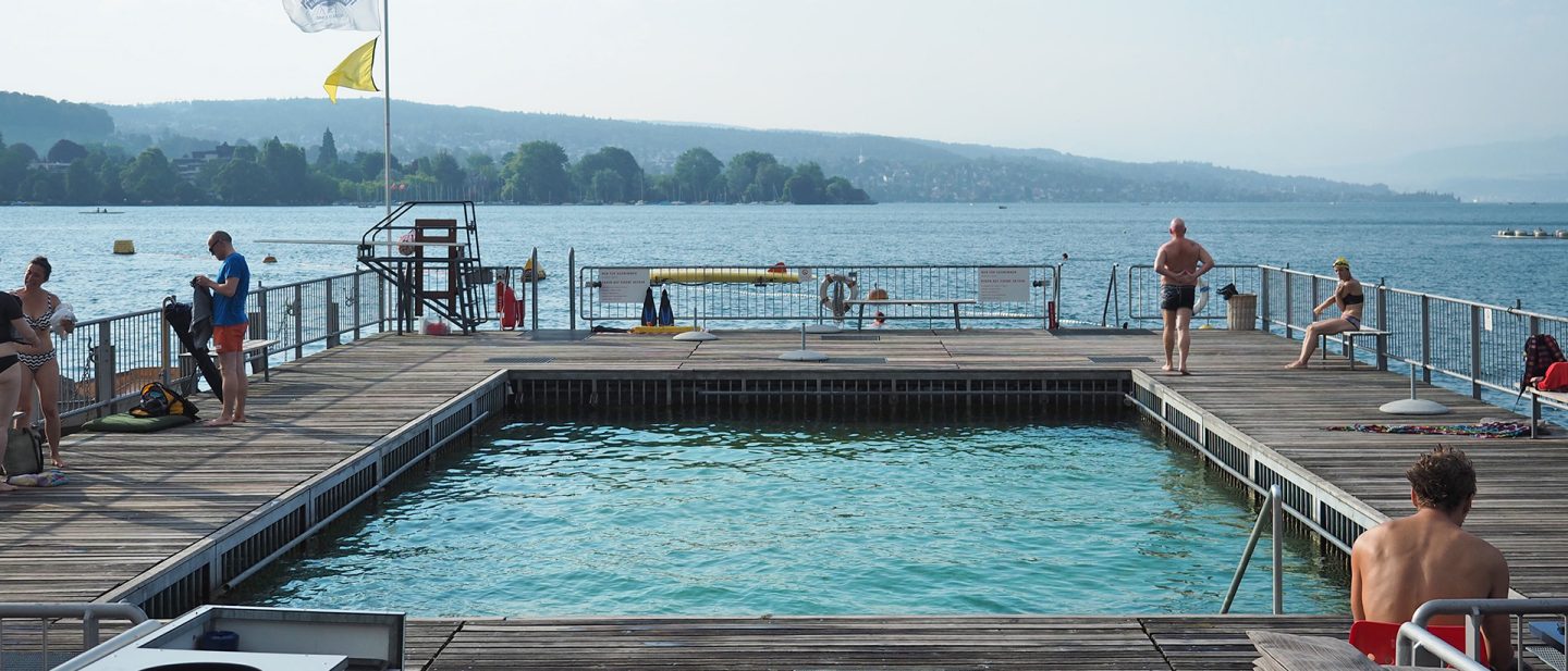 People relaxing on a lakeside wooden pier on a sunny day with clear blue waters