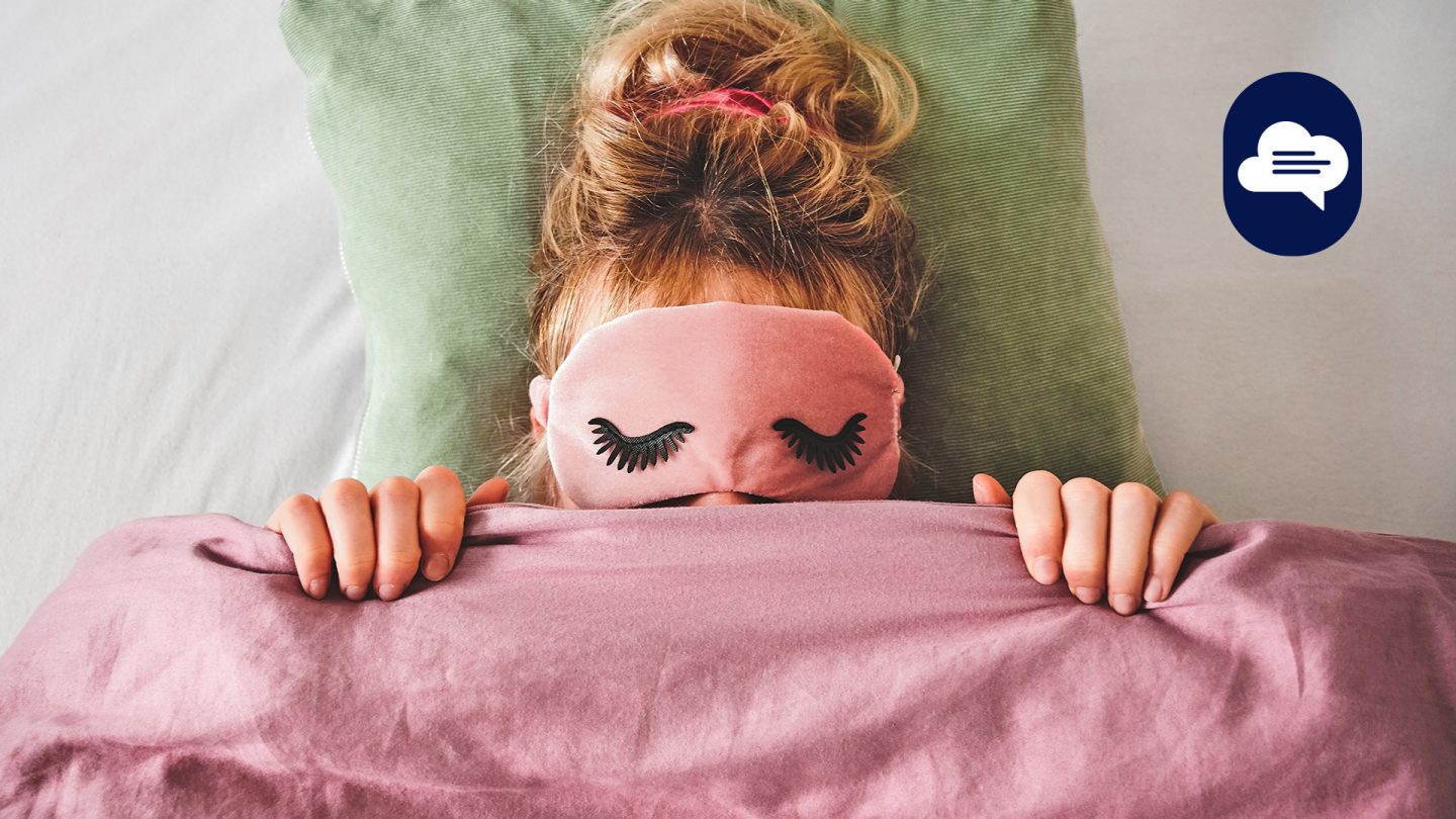 Frau mit Schlafmaske und Decke in Pastellfarben, eingekuschelt im Bett