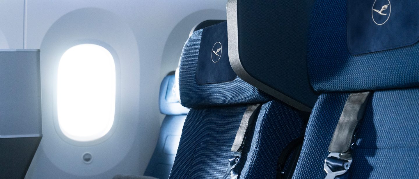 View of an airplane window with two Allegris seats in front, featuring the Lufthansa logo.