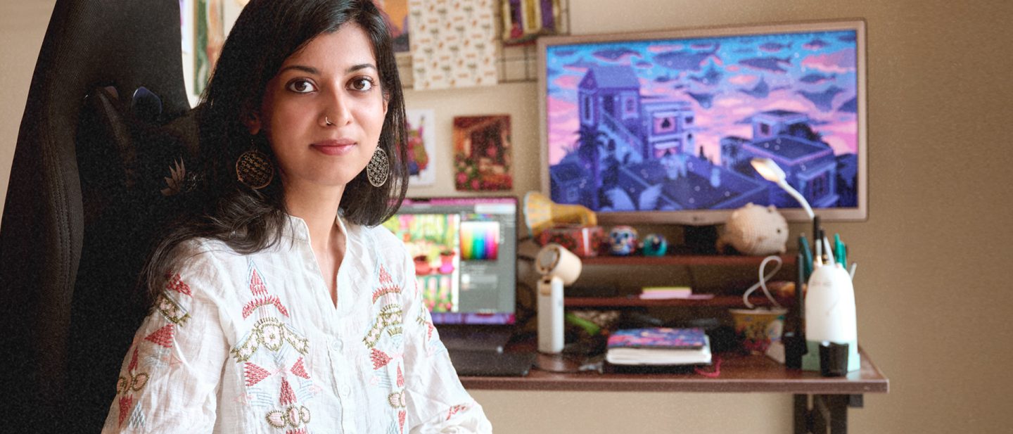 Chaaya is shown at her workspace. In the background you can see a desk with a monitor. She is looking into the camera.