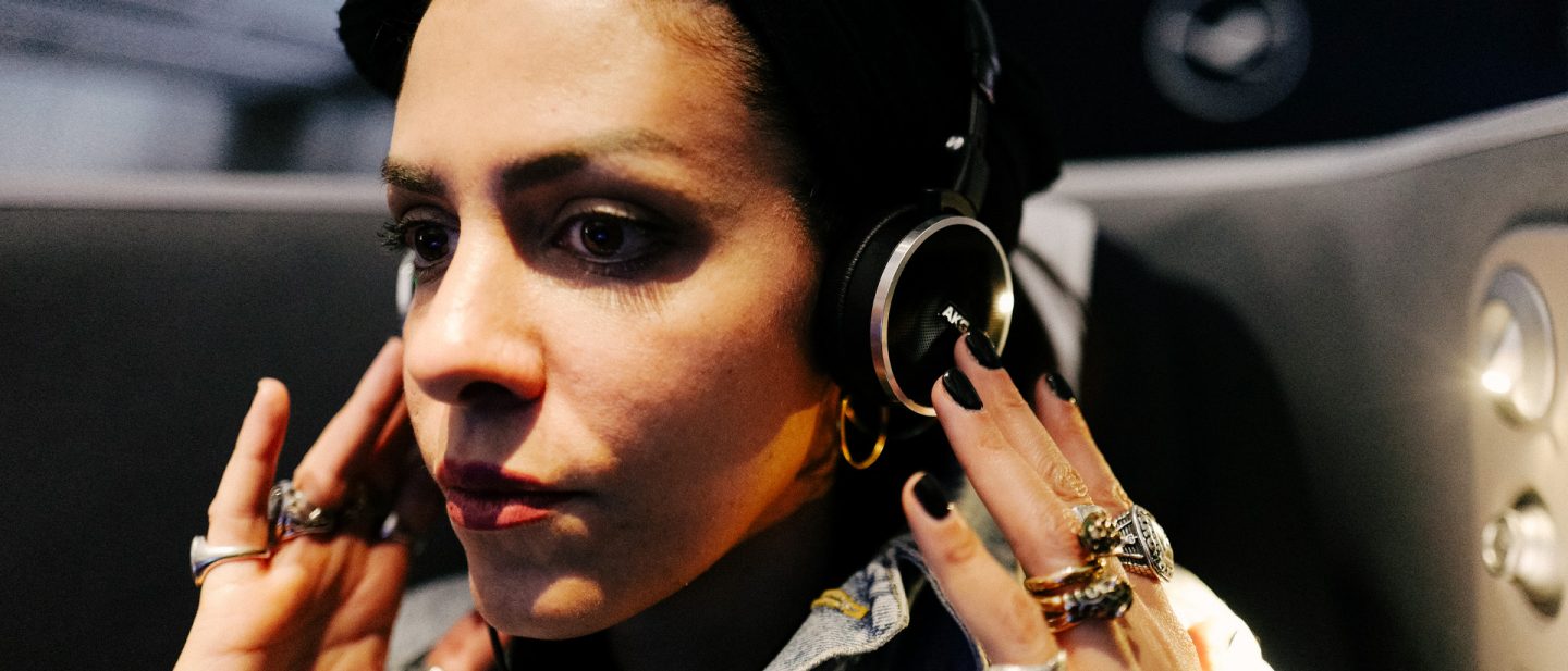 Close-up of a woman with dark hair and striking jewelry putting on headphones in an airplane cabin
