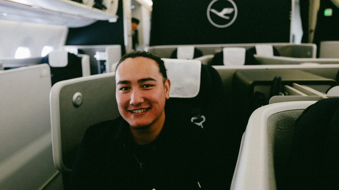 Jacob Chan is sitting in the business class of an airplane with the Lufthansa logo in the background
