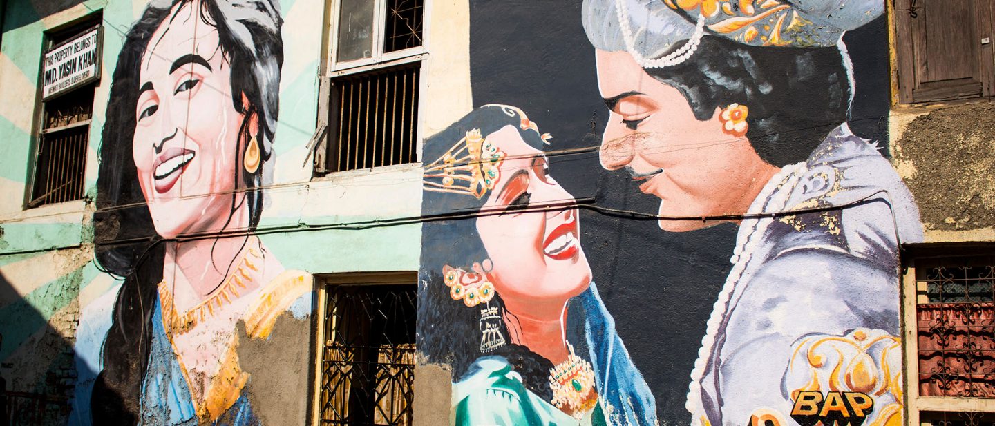Large-scale murals depicting figures from Indian films cover a building facade in Mumbai.