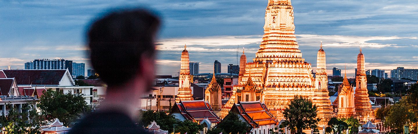 The illuminated Wat Arun temple in Bangkok, seen over a person's shoulder