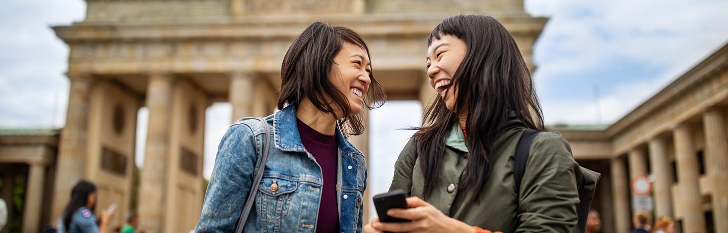 Two laughing women in front of the Brandenburg Gate.