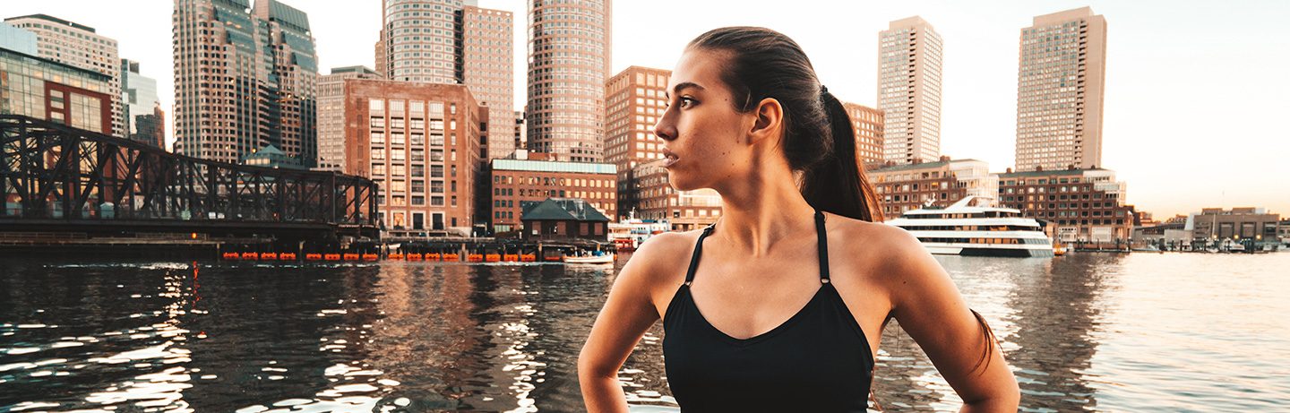 Sportily dressed woman at Boston Harbor in front of the skyline in the warm evening light