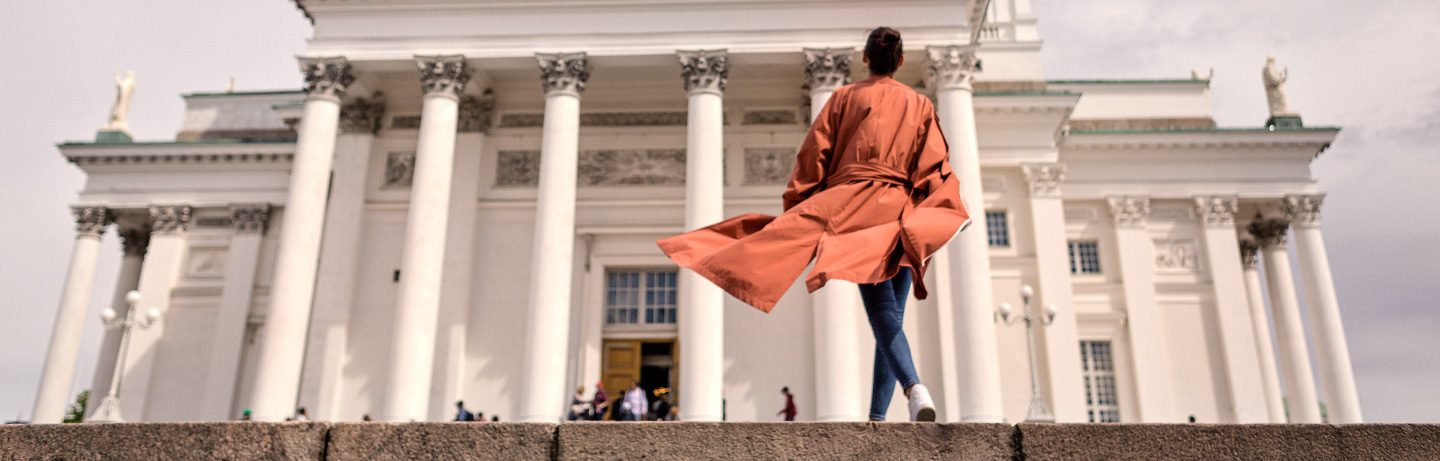 A person in an orange coat walks towards the steps of the Helsinki Cathedral