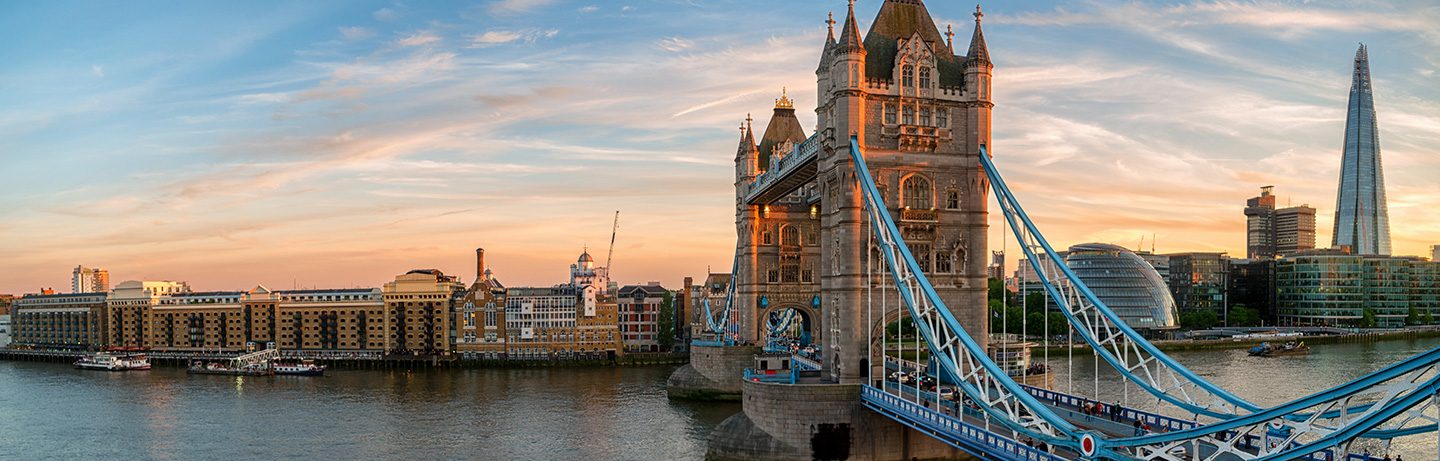 Tower Bridge spanning a river, surrounded by historic and modern buildings in the warm light of sunset.