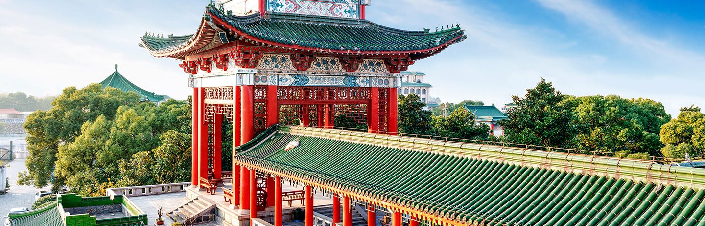 Historic Chinese temple with red columns, ornate architectural details, and green-tiled roofs, surrounded by trees in Beijing.