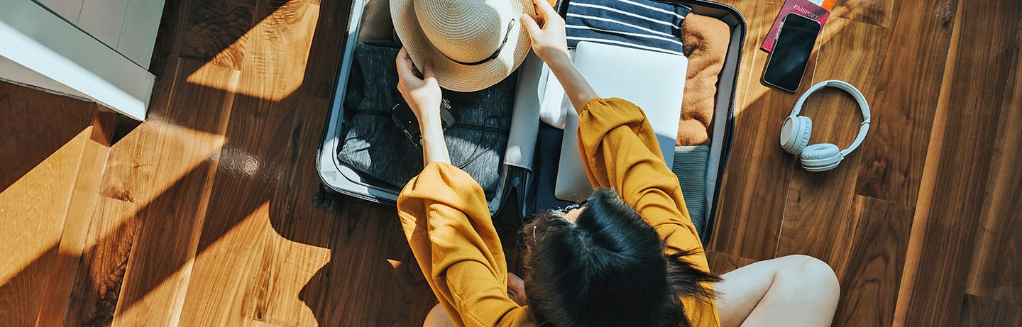  Person carefully packing a suitcase, with a hat and travel essentials beside it