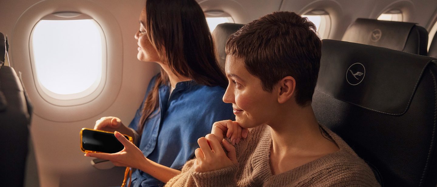 Zwei Frauen sitzen lächelnd in einem Flugzeug am Fenster