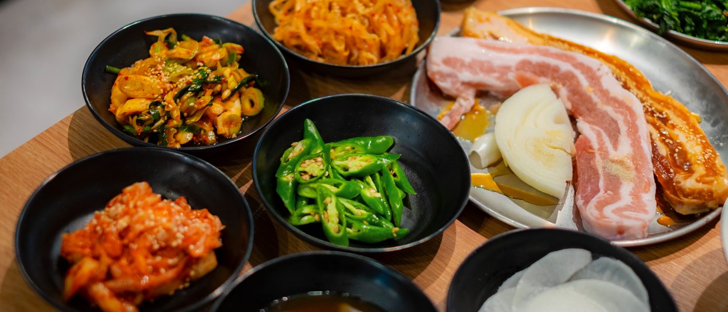 Verschiedene koreanische Gerichte, darunter Kimchi, frisches Gemüse und mariniertes Fleisch, auf einem Holztisch