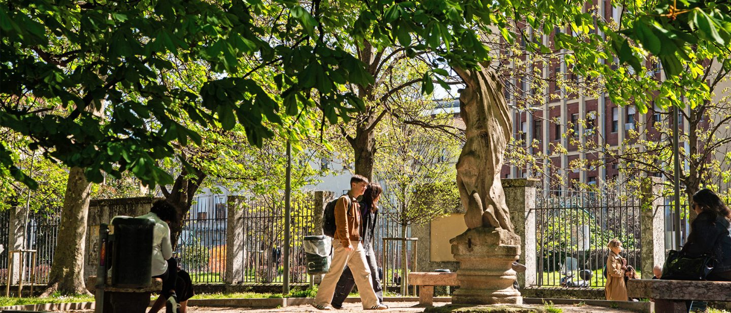 Sonniger Park mit Bäumen, Statue und spazierenden Menschen in Bellano, Mailand