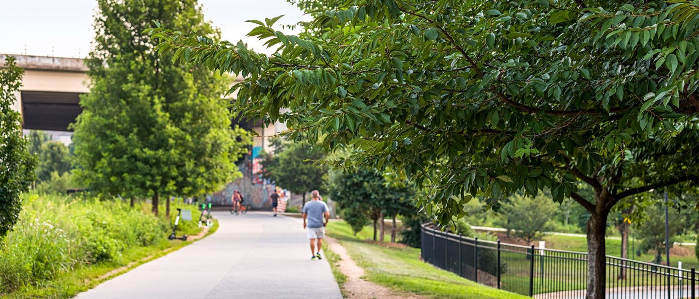 Fußgänger und E-Scooter auf der gepflasterten Atlanta BeltLine, gesäumt von grünen Bäumen