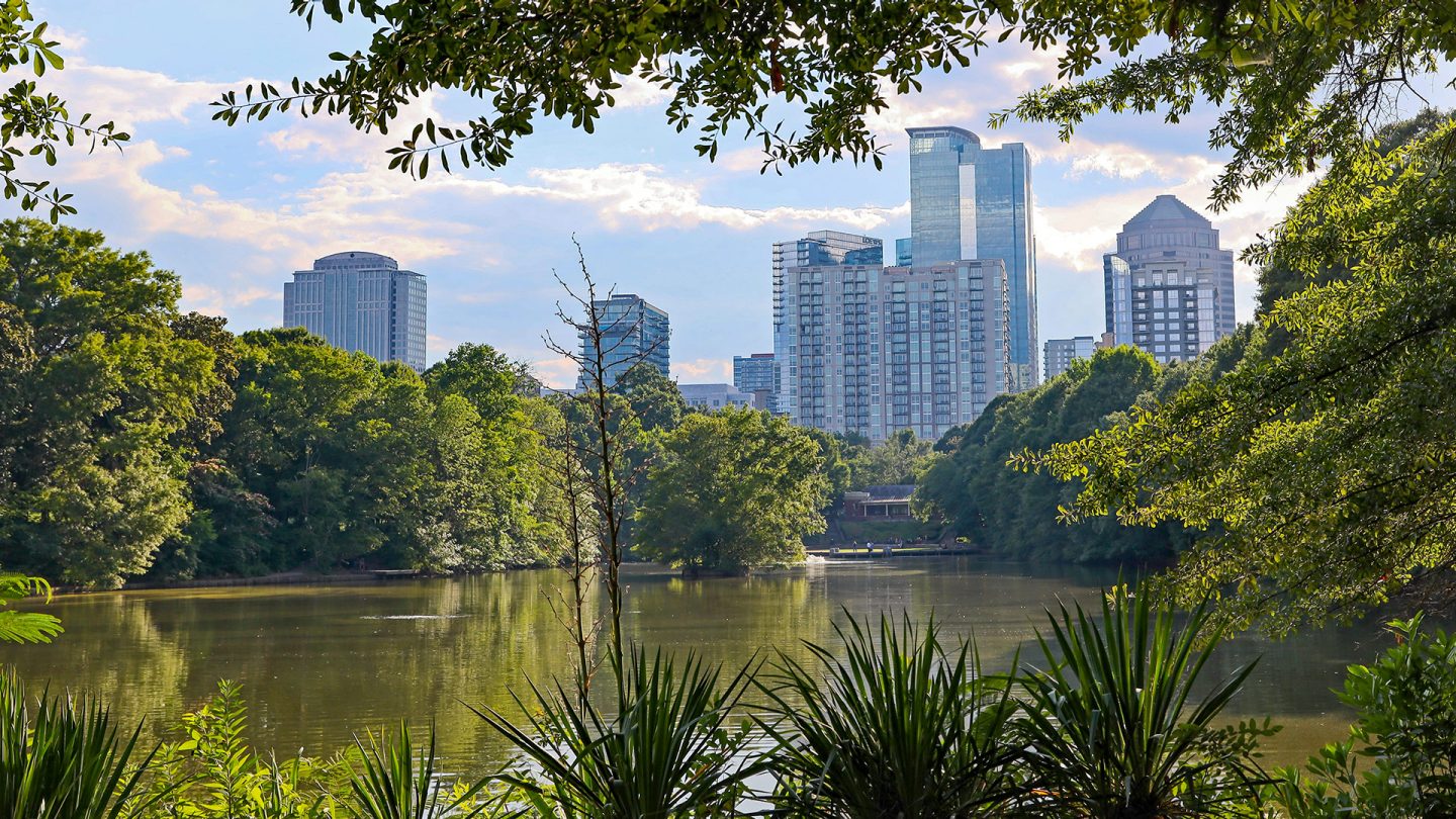 Skyline von Midtown Atlanta hinter einem See im Piedmont Park, eingerahmt von grünem Laub