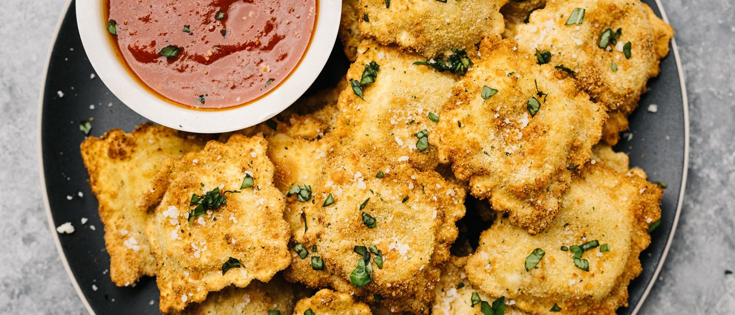 Knusprig frittierte Ravioli mit Kräutern und Parmesan auf einem Teller mit Marinara-Dip.