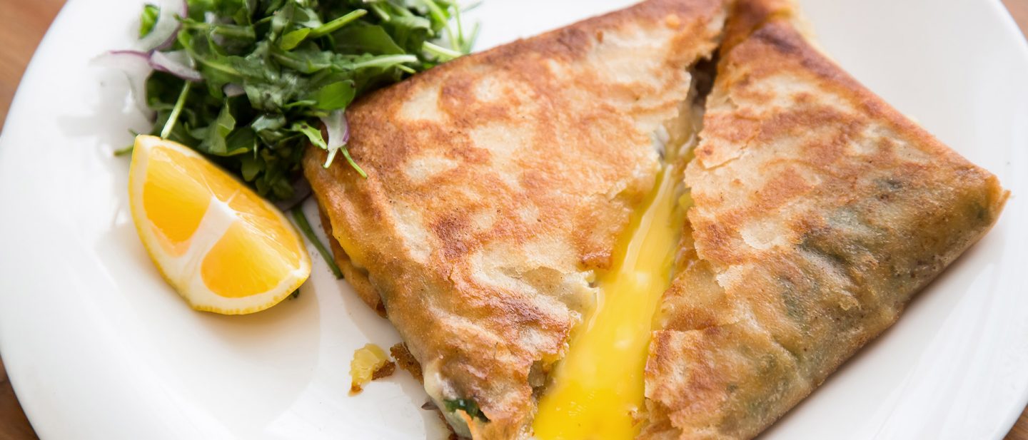 Goldbraunes gefülltes Fladenbrot mit geschmolzenem Käse, serviert mit einer Zitronenspalte und frischem Gemüse auf einem weißen Teller.