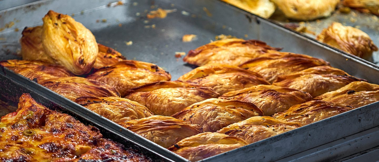 Frisch gebackene, goldbraune Pastizzi auf einem Backblech in einer Bäckerei