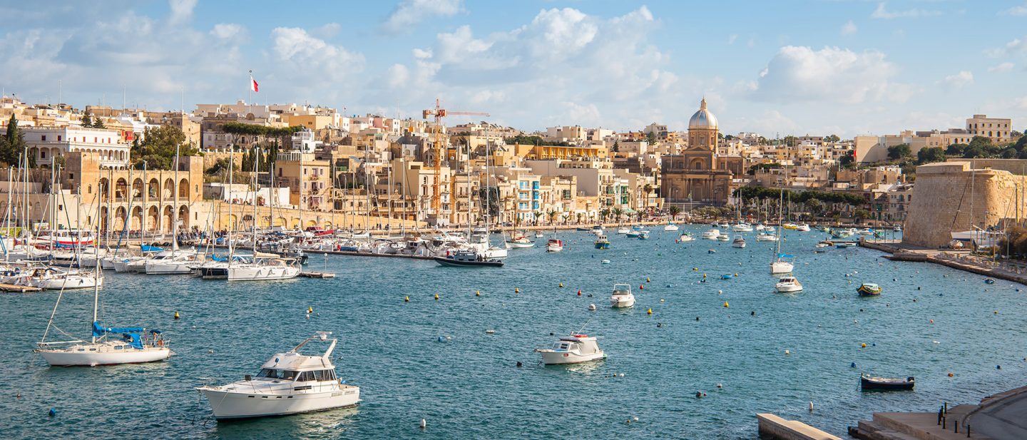 Blick vom Wasser auf historische Festungsanlagen und eine Stadt am Hafen mit verschiedenen Booten