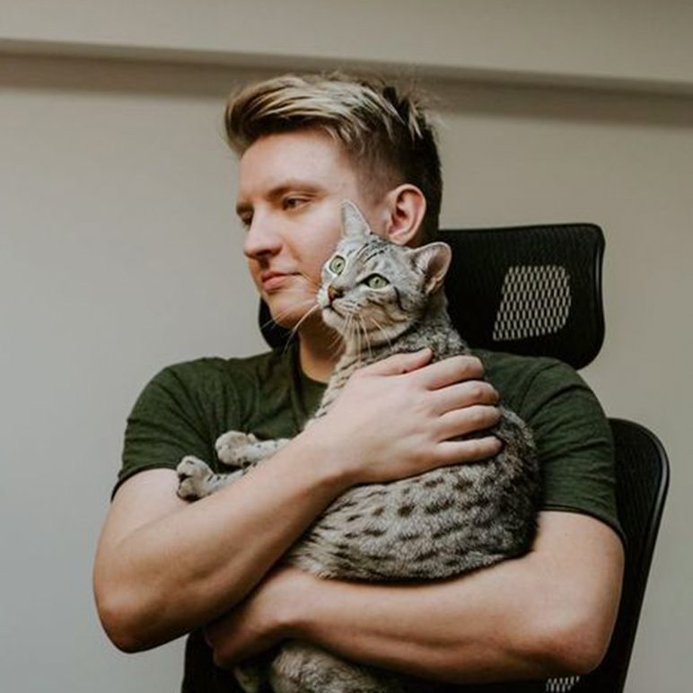  Filip Hodas sitzt auf Bürostuhl und hält eine grau getigerte Katze im Arm