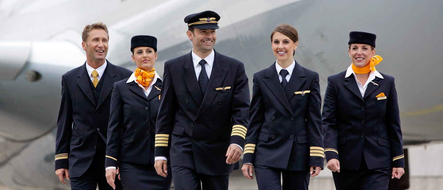 Pilot und Flugbegleiter:innen gehen gemeinsam über das Vorfeld vor einem Flugzeug.
