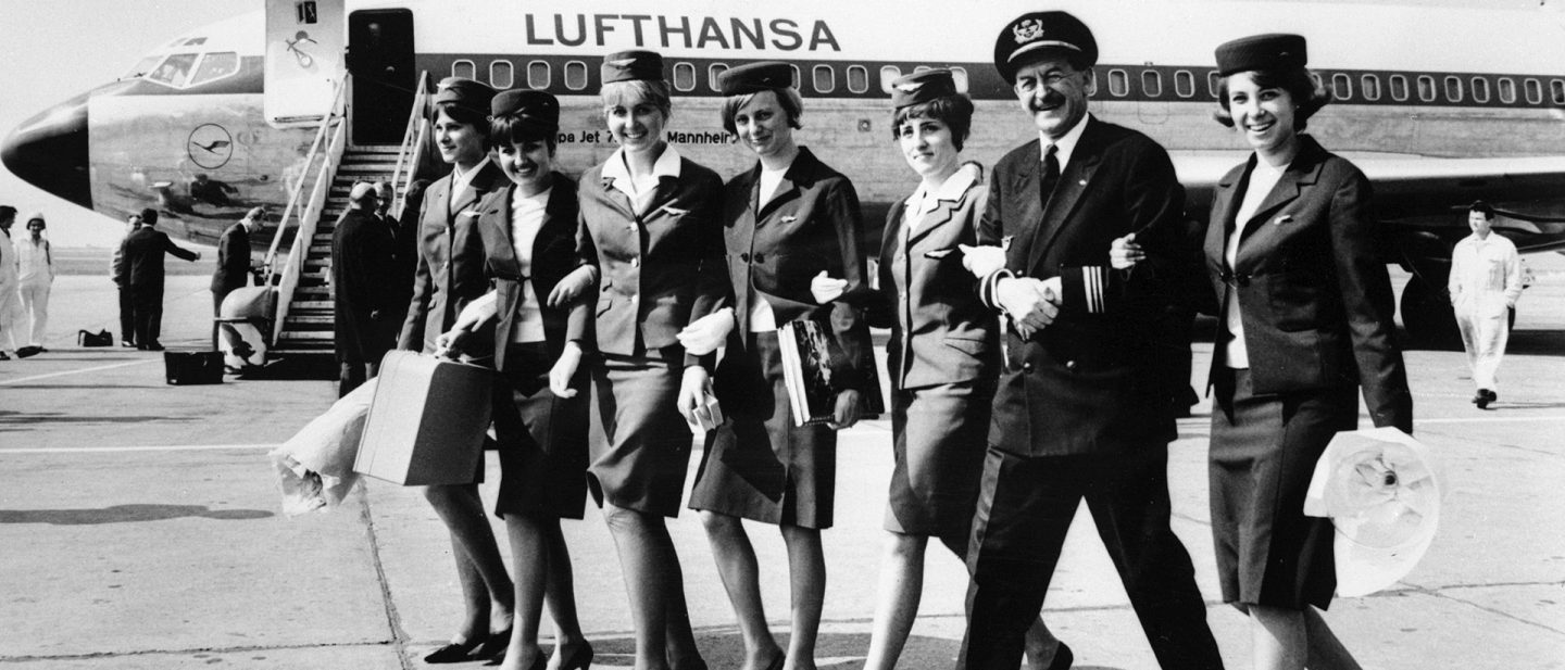 Historische Lufthansa Crew mit Pilot und Flugbegleiterinnen läuft vor einem Flugzeug.