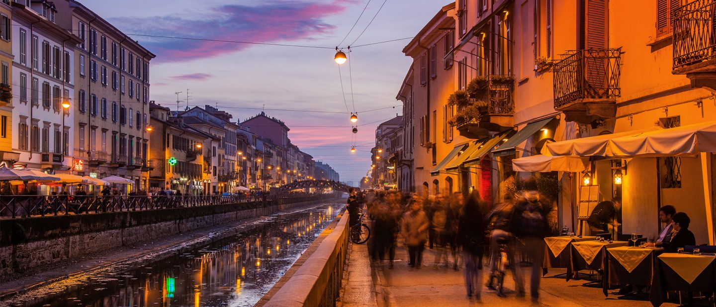 Abendstimmung im Mailänder Navigli-Viertel mit beleuchteten Restaurants am Kanal und flanierenden Menschen