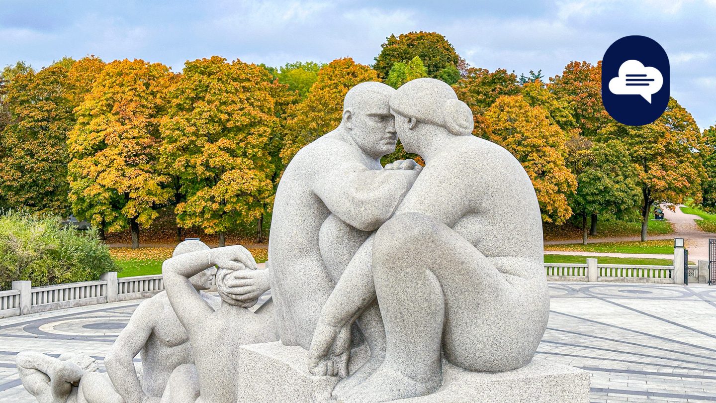 Skulptur von sich umarmenden Figuren vor einem Hintergrund herbstlicher Bäume im Vigeland-Skulpturenpark