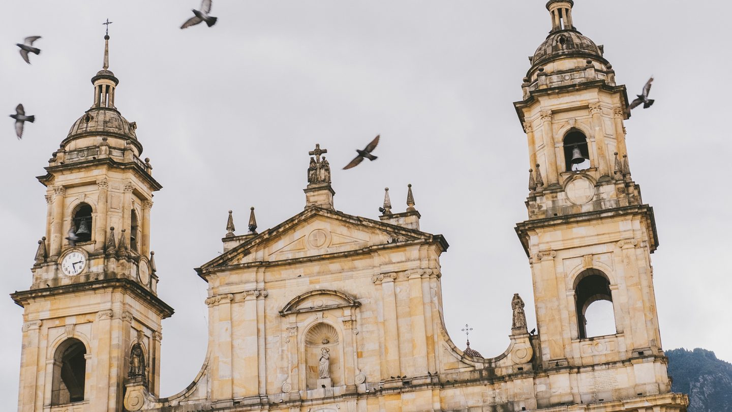 Die Fassade der sandfarbenen Kathedrale von Bogotá mit drei Türmen und Vögeln am Himmel