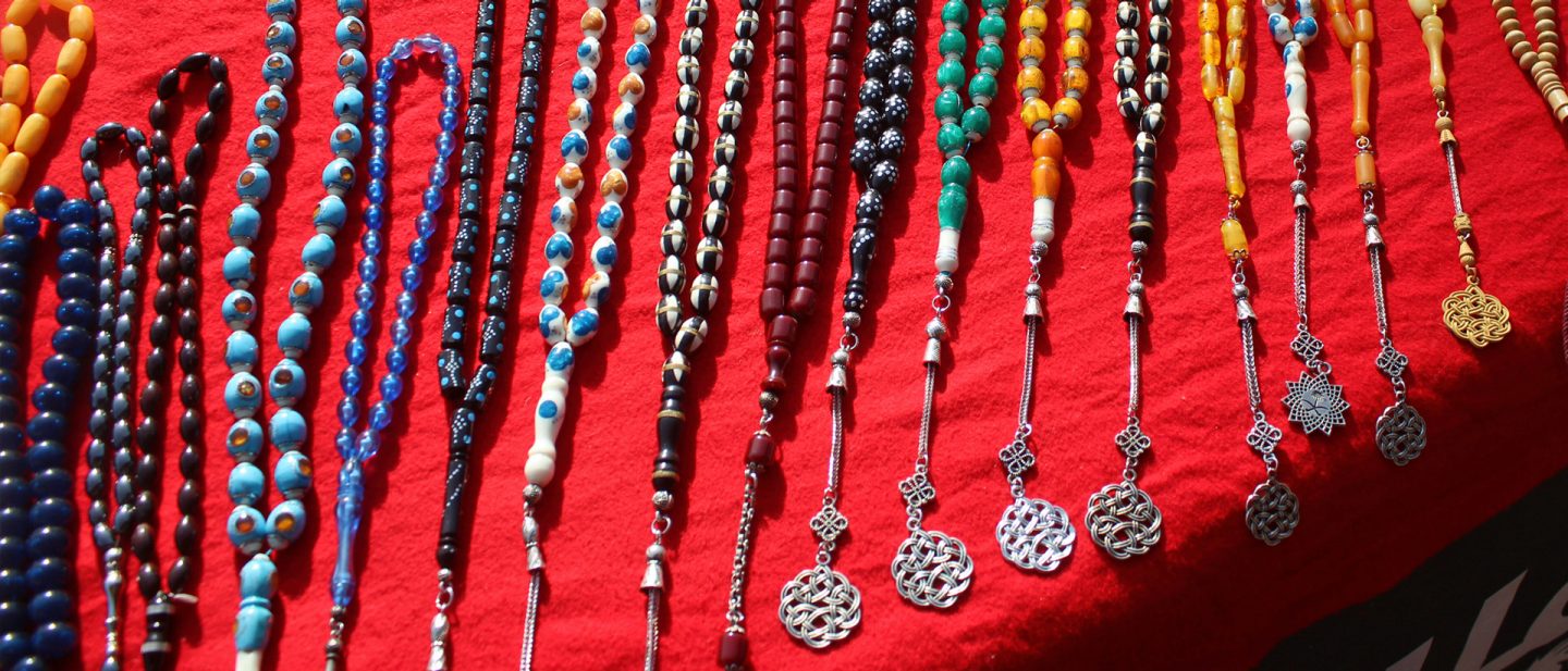 Bunte Gebetsketten Masbaha Tesbih aus Perlen und Steinen mit Silberanhängern auf rotem Tuch auf einem Flohmarkt in Riad