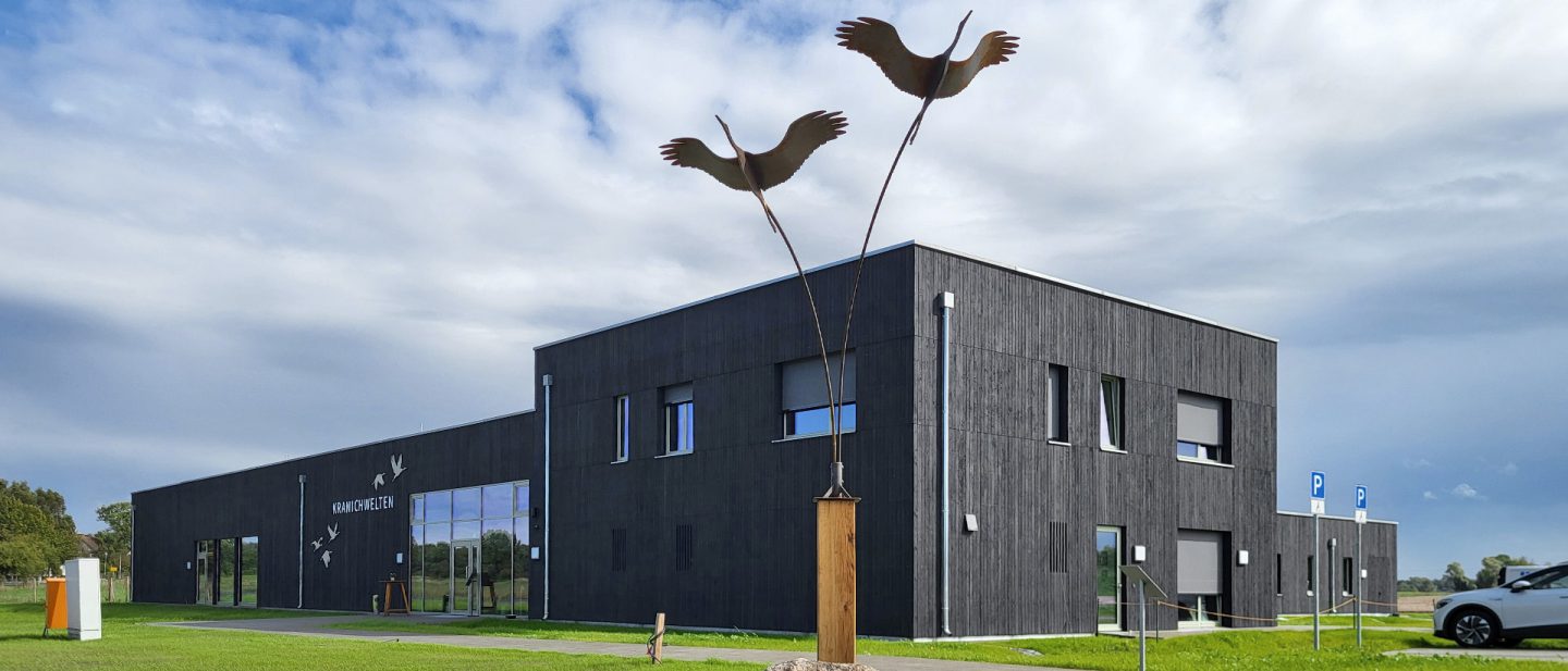 Ein modernes schwarzes Gebäude mit einer Skulptur fliegender Kraniche im Vordergrund
