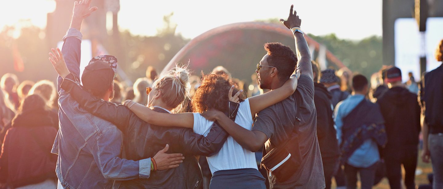 Vier Personen im Vordergrund stehen Arm in Arm vor einer großen Menschenmenge bei einem Festival