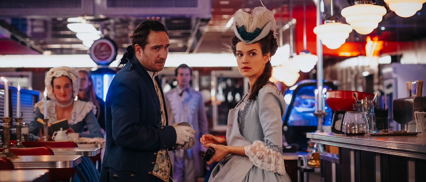 Szene mit Emilia Schüle im barocken Kostüm in einem modern wirkenden Diner