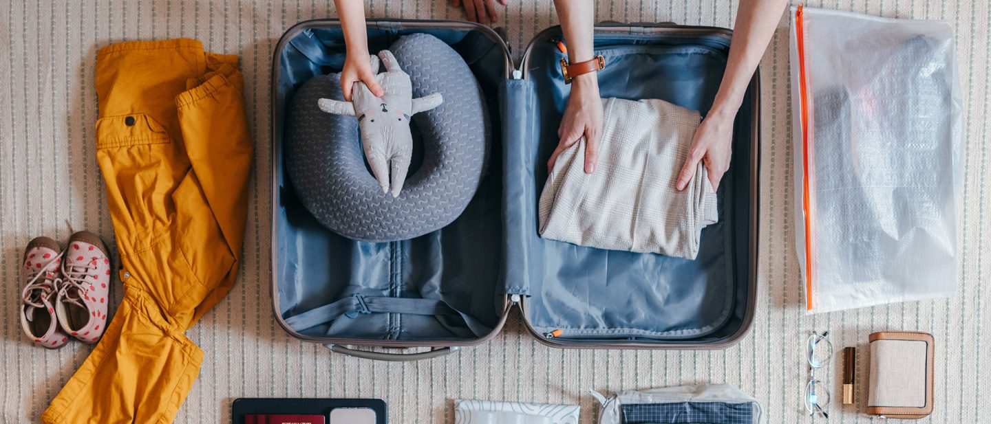 Offener Koffer: Kinderkleidung und Kuscheltier werden eingepackt