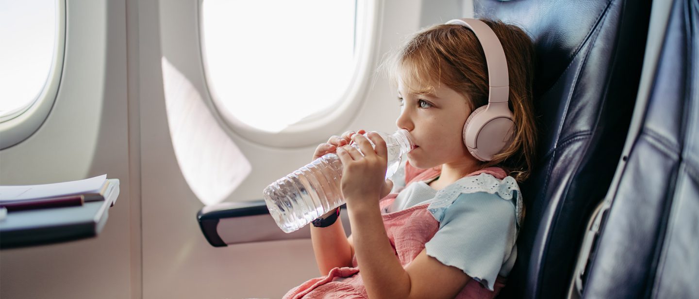 Mädchen mit Kopfhörern trinkt Wasser im Flugzeug