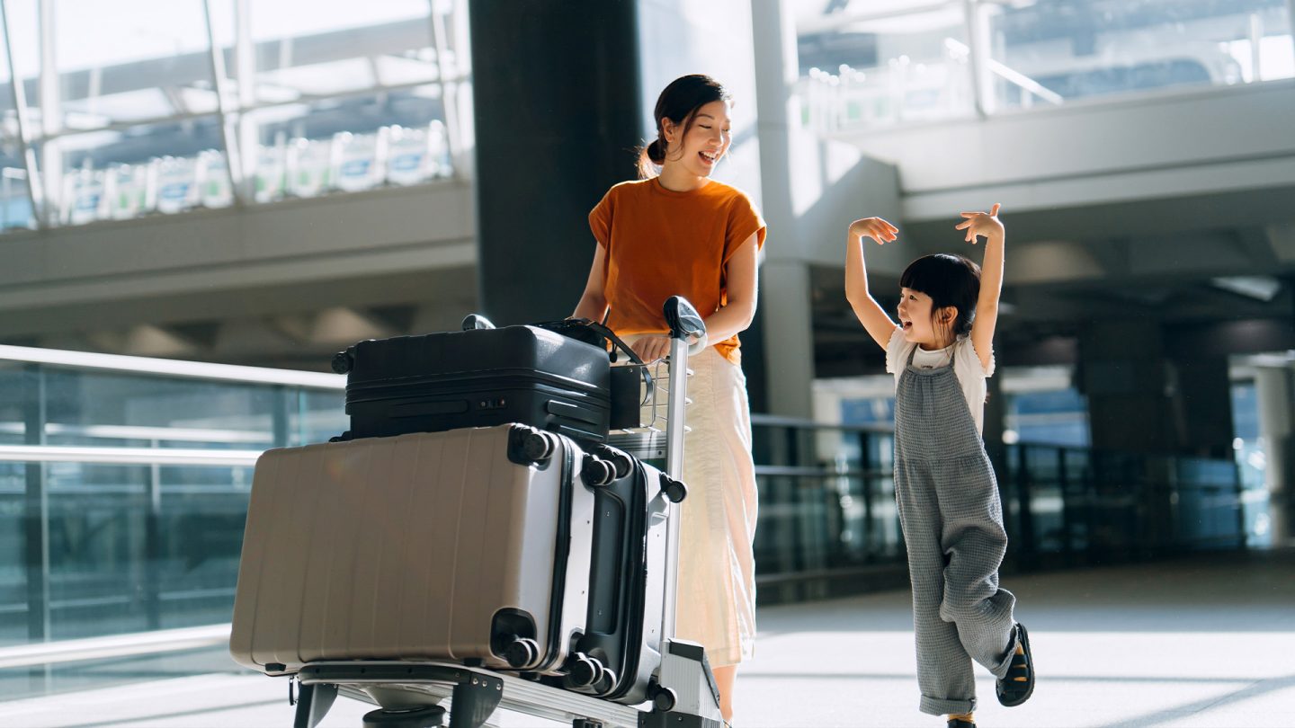 Mutter mit Kind und Koffern lachend im Flughafen unterwegs