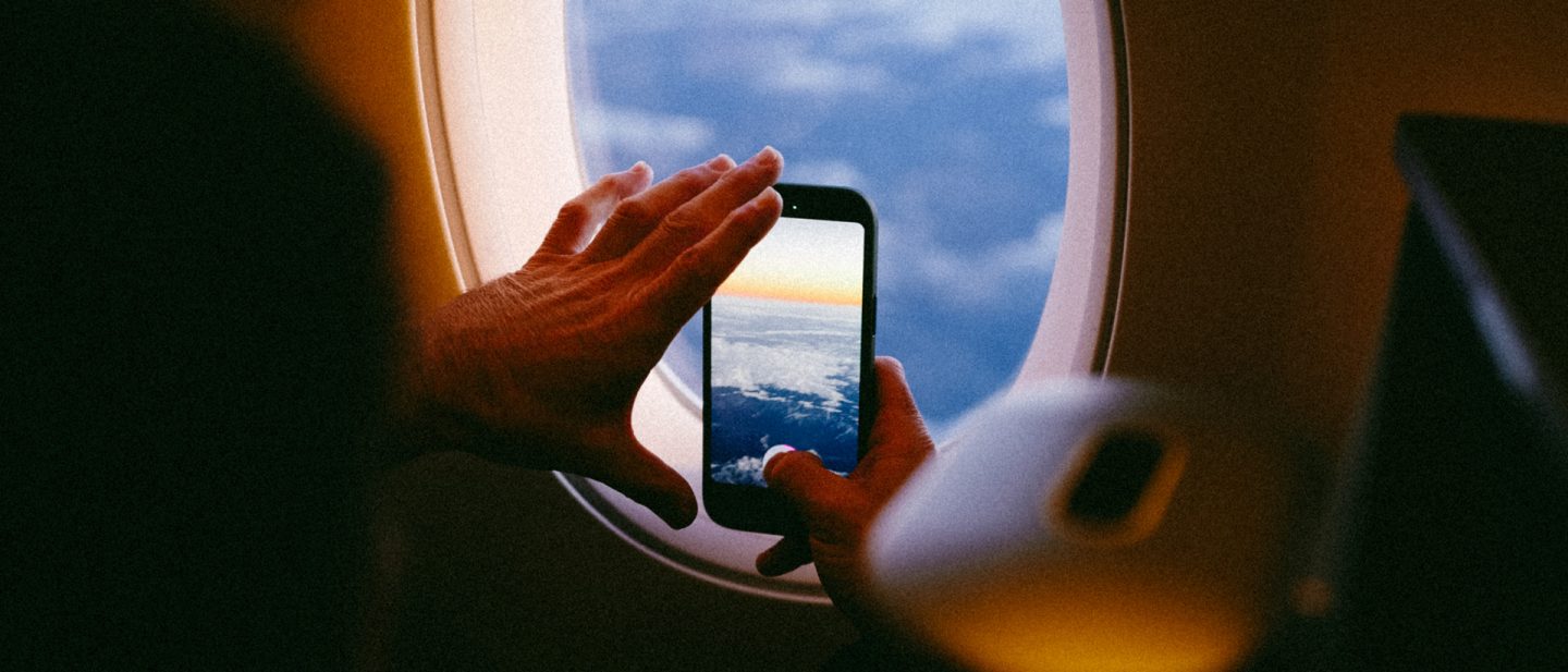 Person macht ein Foto von Wolken und Sonnenuntergang aus dem Flugzeugfenster mit dem Smartphone während des Fluges.