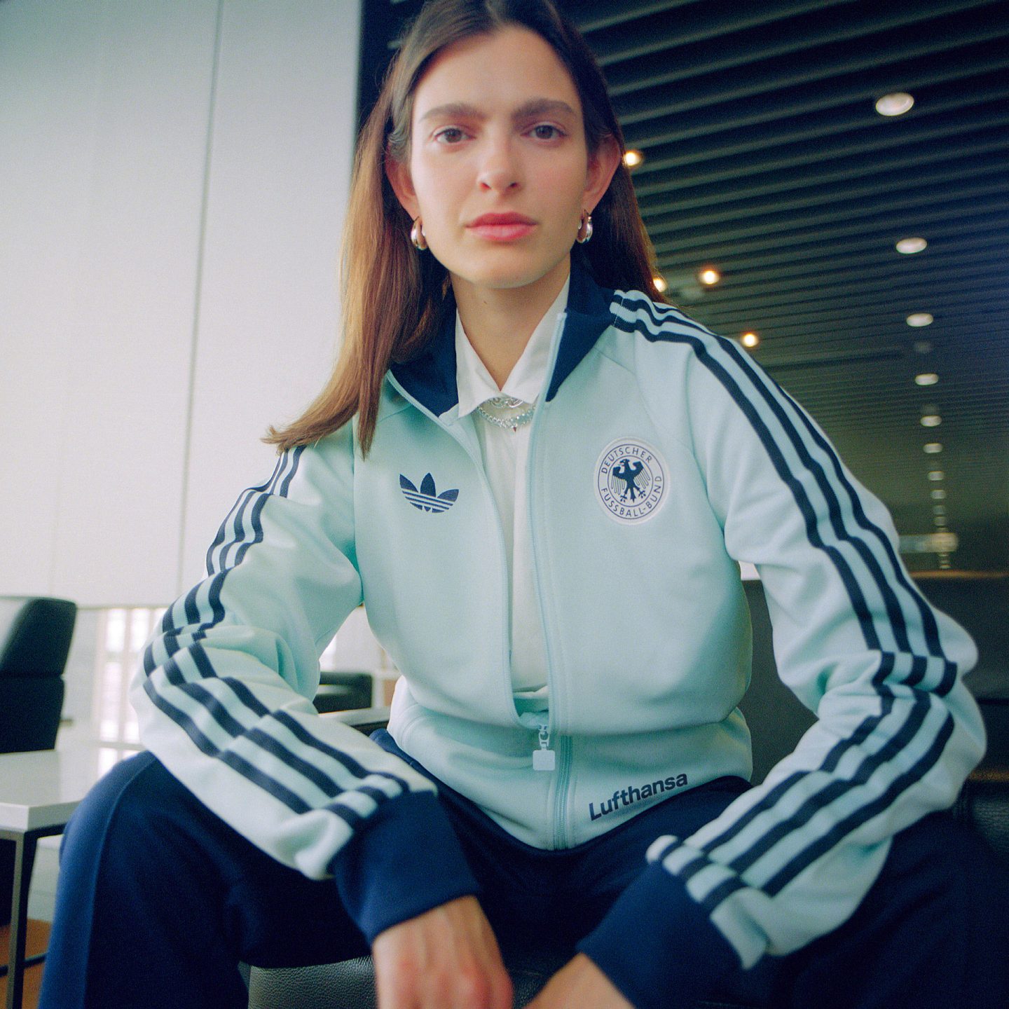 Person trägt einen hellblauen Trainingsanzug mit Logos von adidas, DFB und Lufthansa.